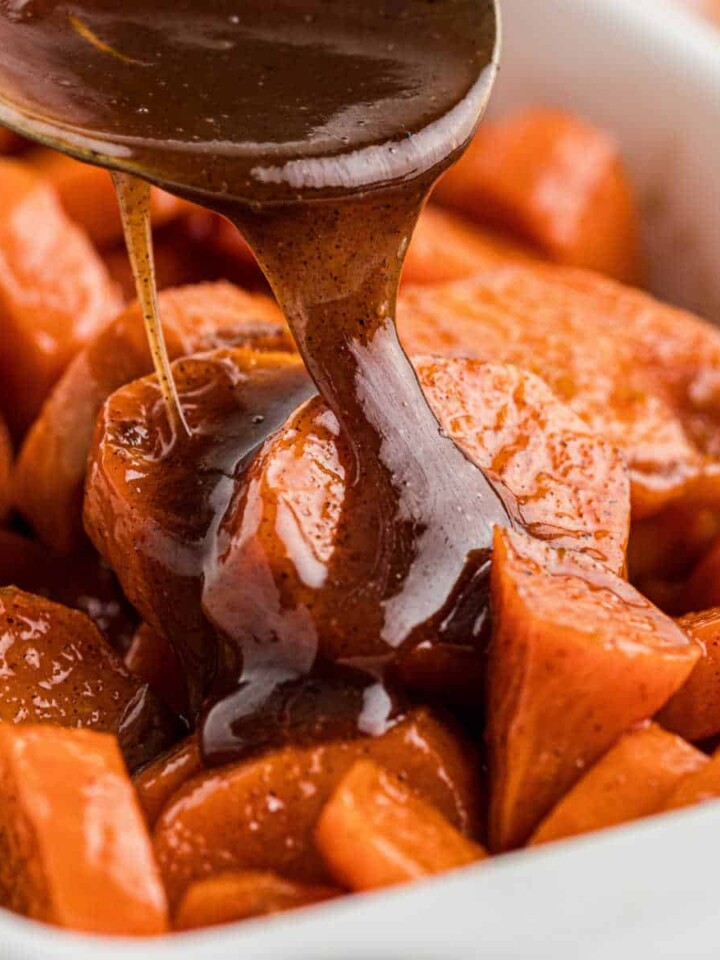 A dish full of yams with a treacle being poured over the top.