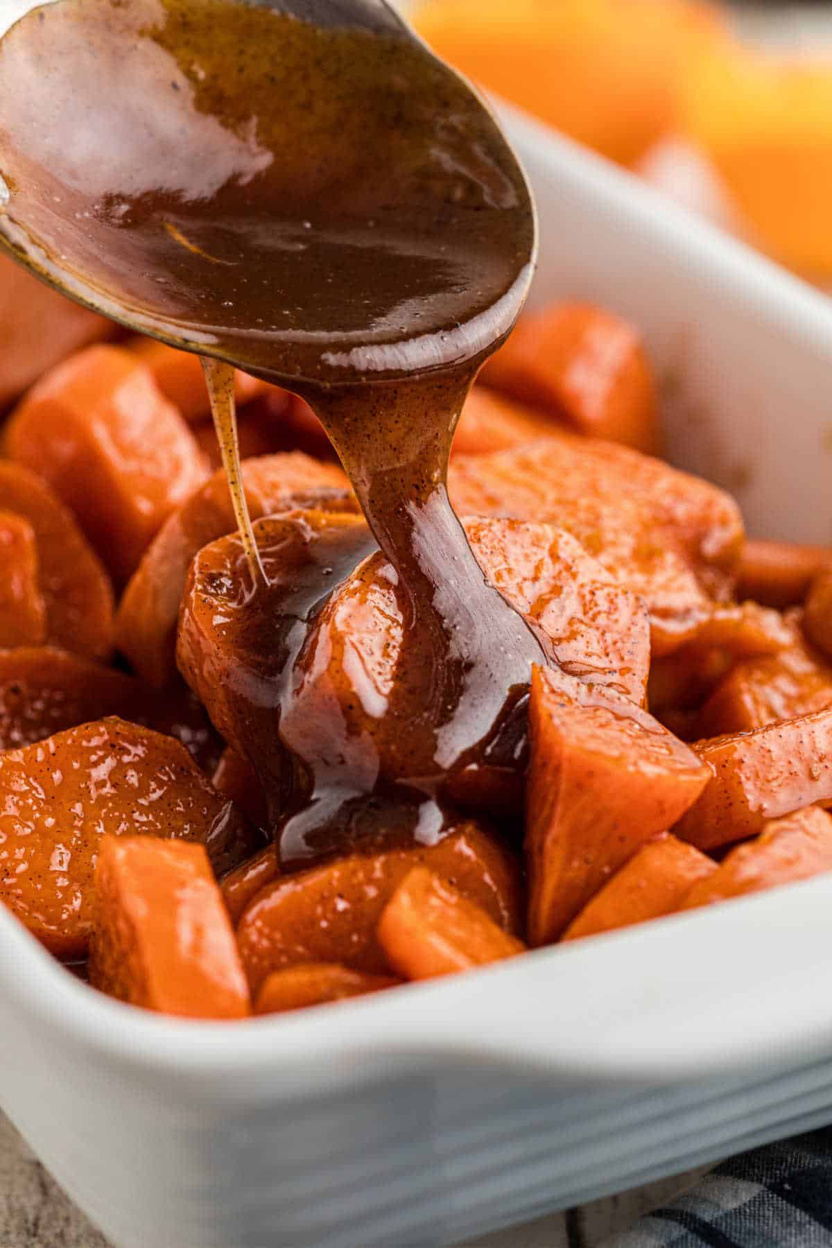 A dish full of candied yams with a treacle being poured over the top.