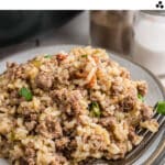 A close up of a plate of dirty rice, with a fork on top. There's text overlay for pinterest.