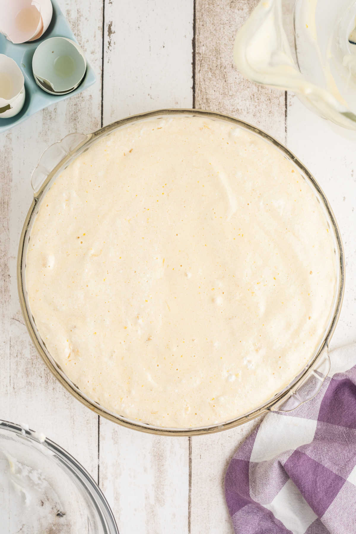 Cake batter on top of pineapple slices in a pie dish.