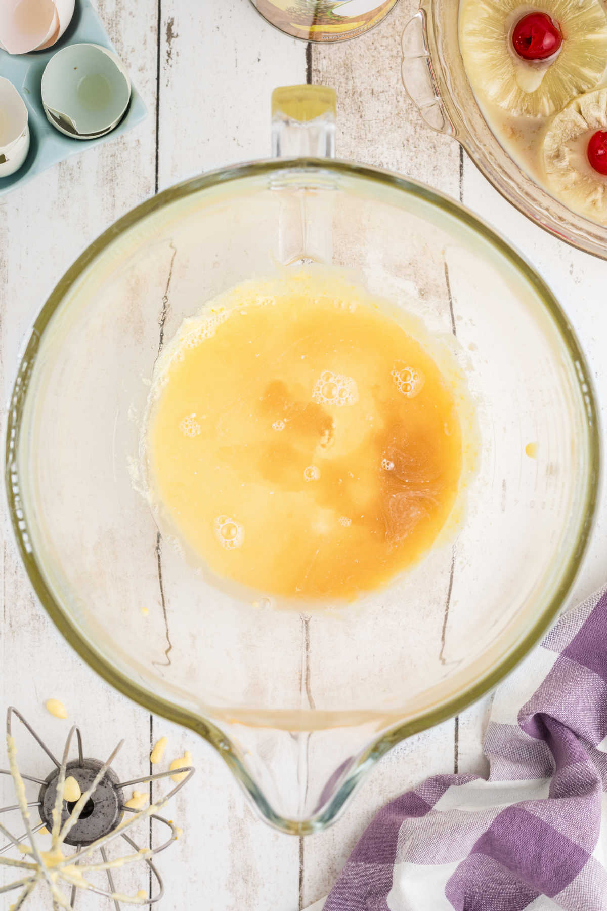 Vanilla and pineapple juice being added to a mixing bowl with butter and sugar.