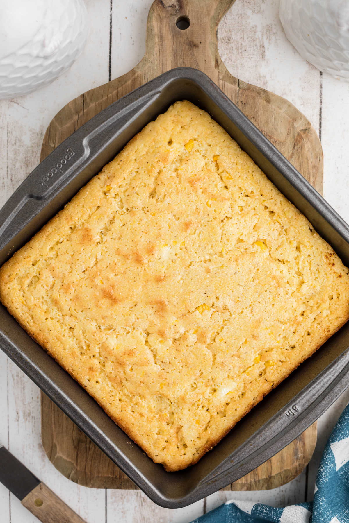 Overhead shot of a cornbread, cooked in a square pan, resting on a wooden board.