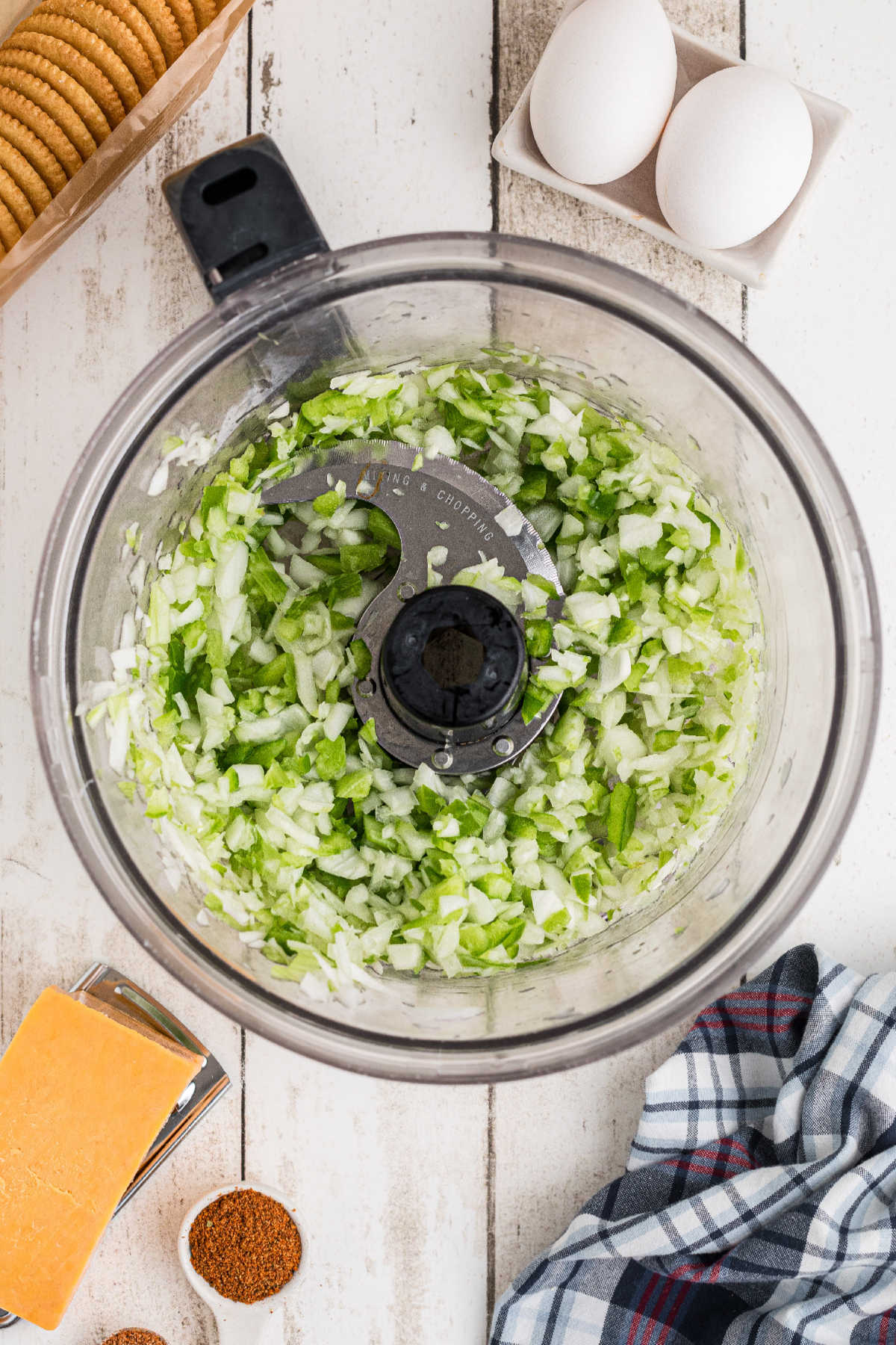 Onion, bell pepper and celery being chopped in a food processor.