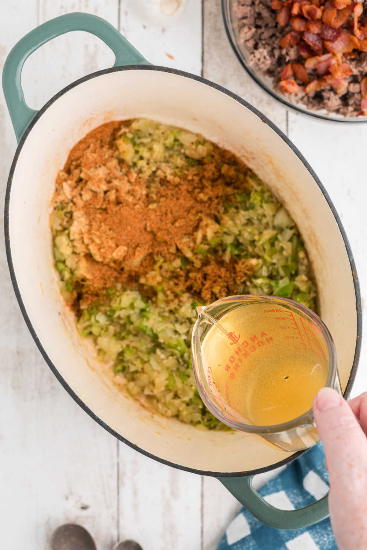 Chicken broth being poured into a pot with veggies and seasoning.