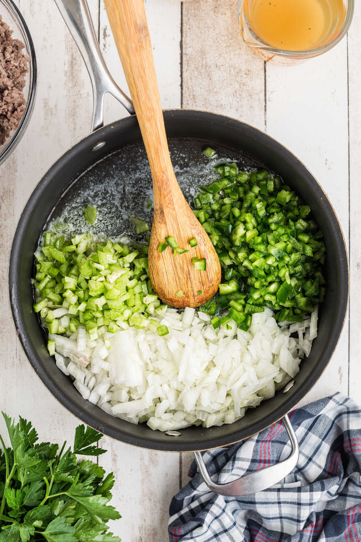 Onions, bell pepper and celery being cooked in a skillet.