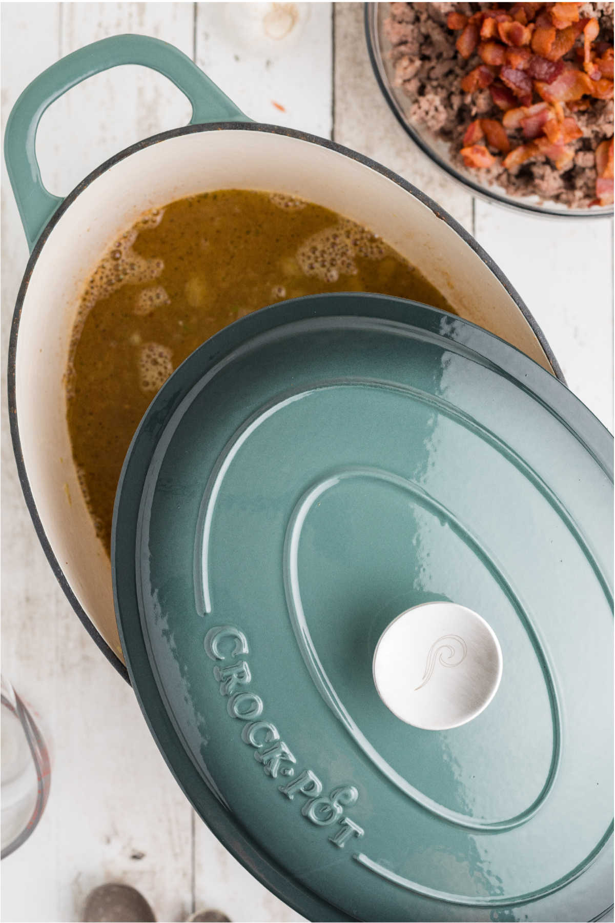 A lid being placed on a large Dutch oven with ingredients about to be simmered.