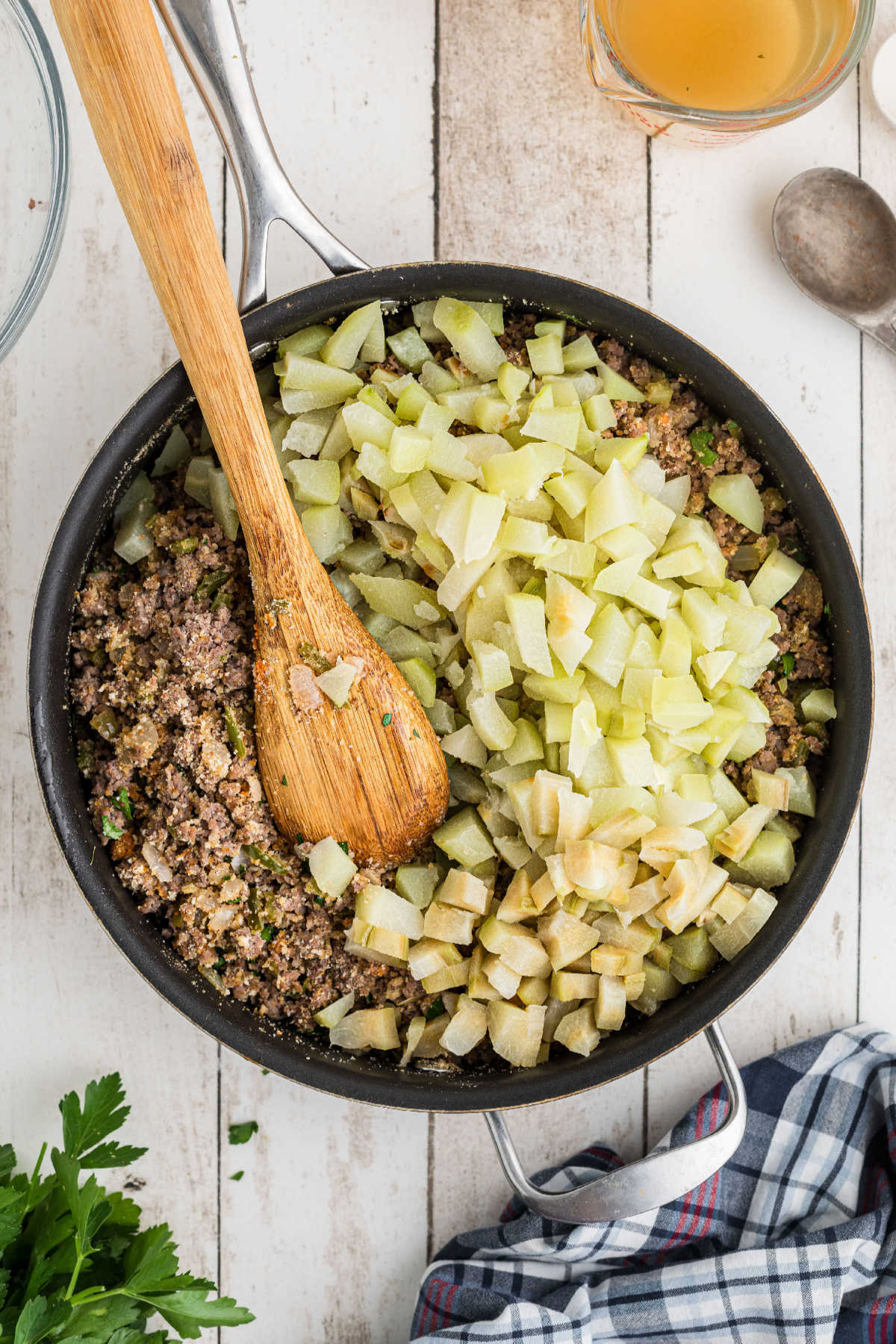 Chopped mirlitons added to a large skillet with meat and veggies.