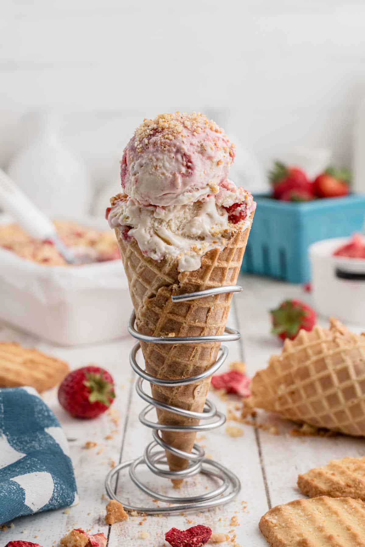 Strawberry Shortcake Ice Cream in a waffle cone, standing up in a wire holder.