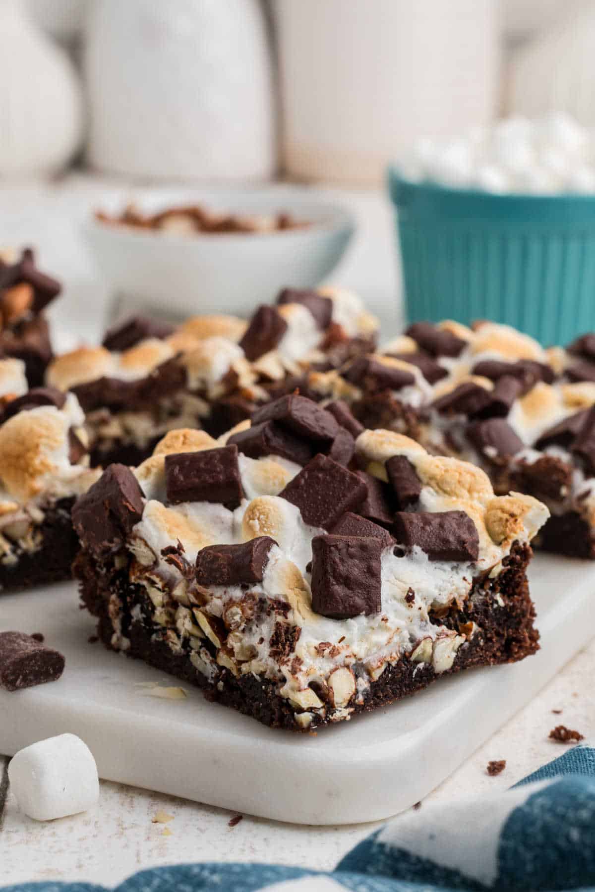 Shot of some rocky road brownies with a blue bowl in the background full of marshmallows.