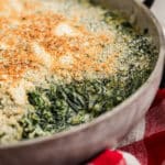 Close up shot of a spinach madeleine dish in a pan with a scoop missing.