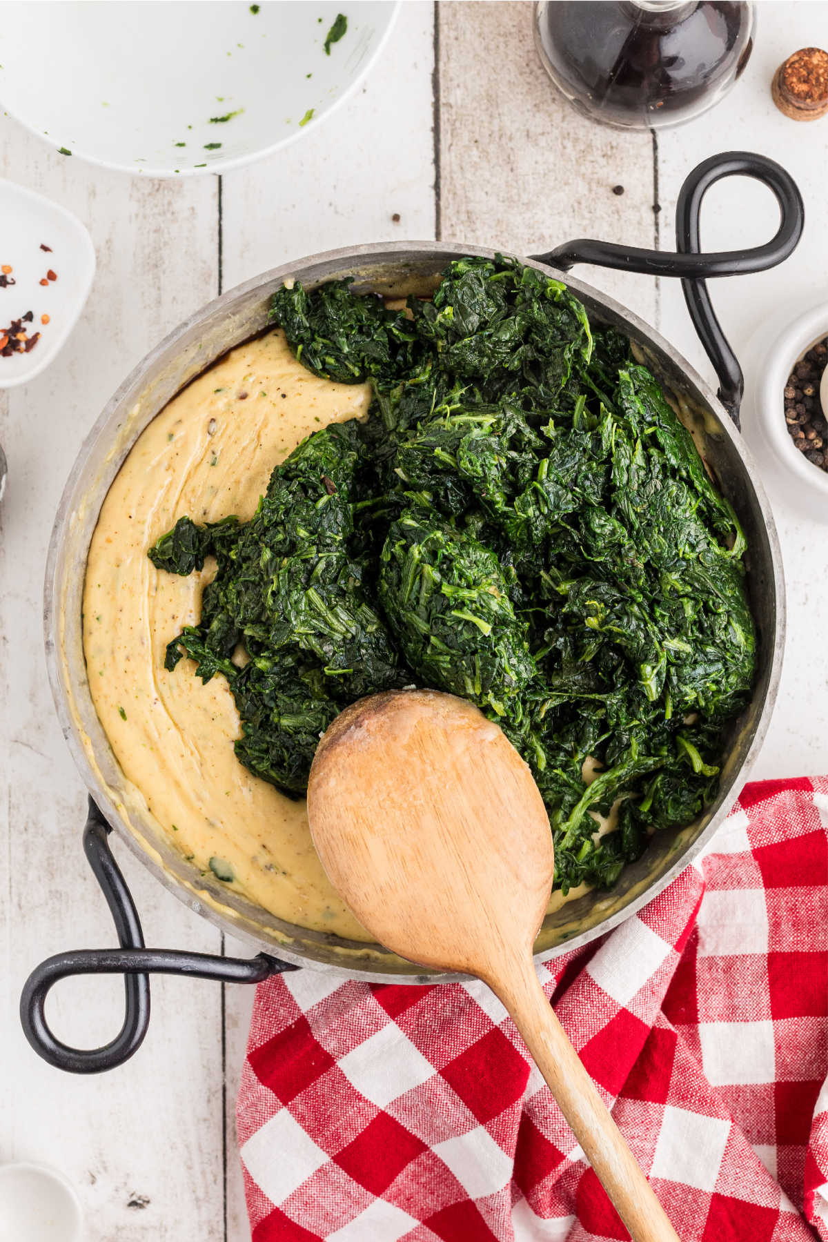 Cooked spinach added to a skillet with a cheese sauce.