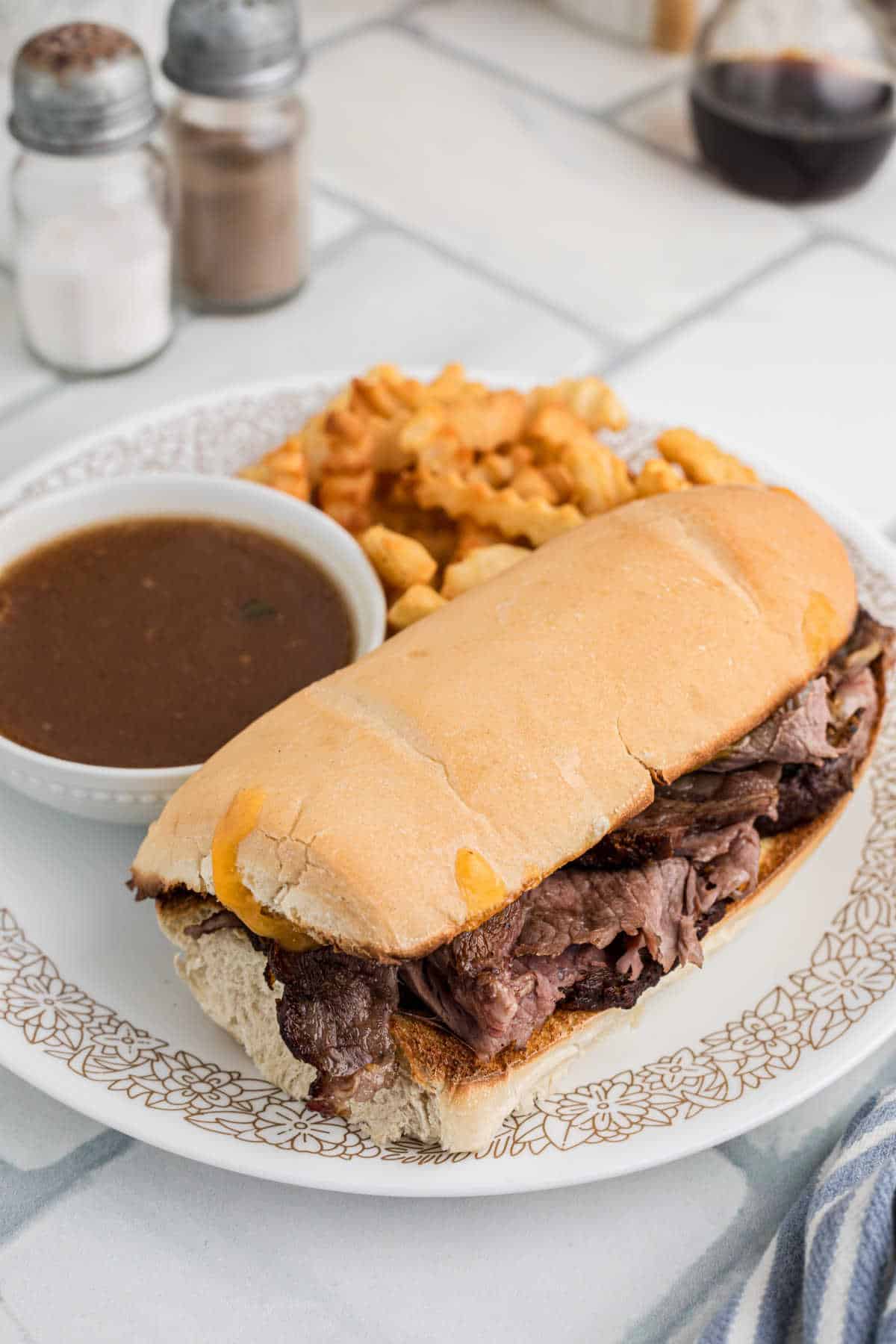 A plate with a large Leftover Prime Rib sandwich, with a bowl of gravy on the side.