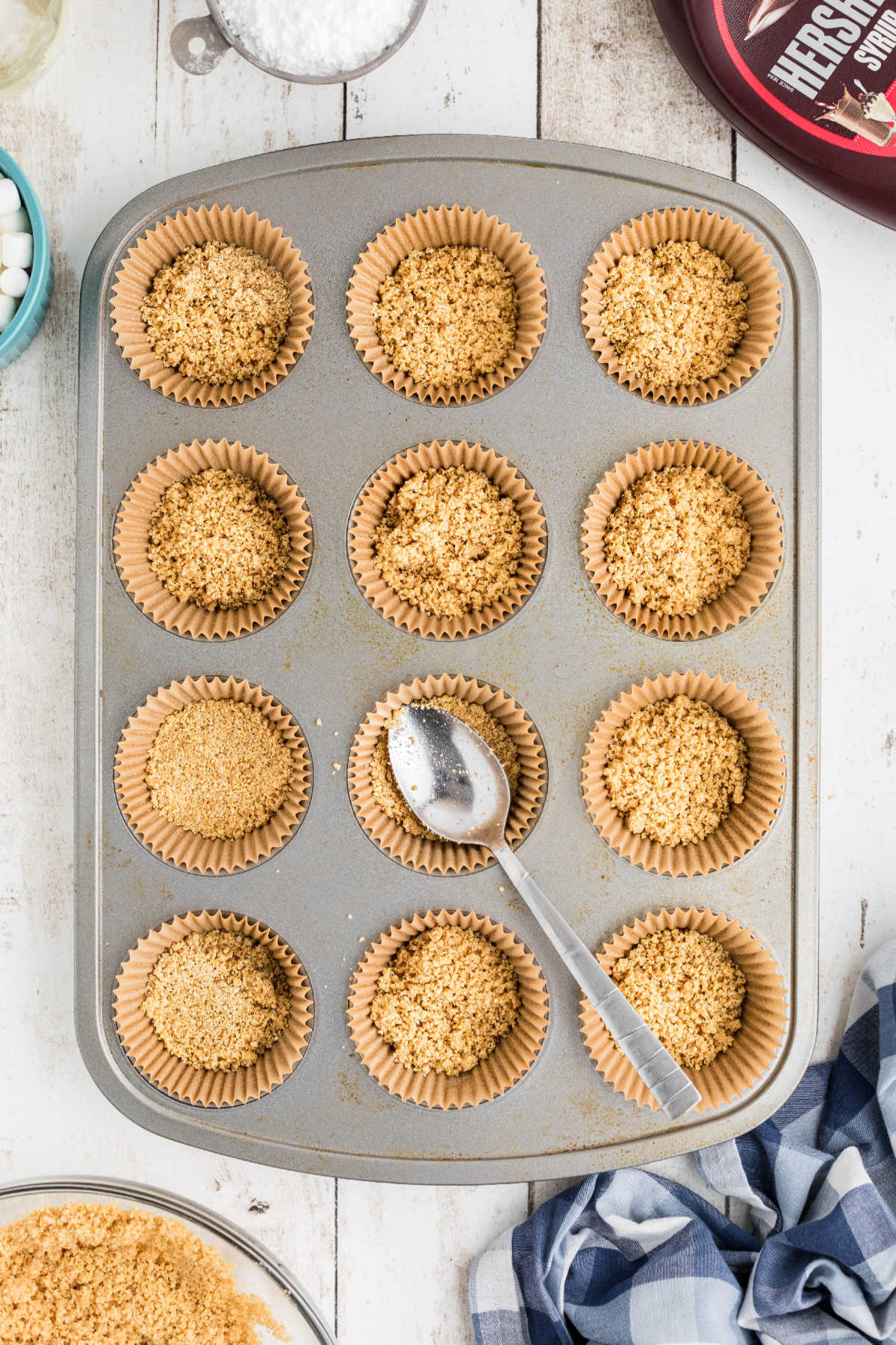 Graham cracker crumbs being pressed into muffin tin.