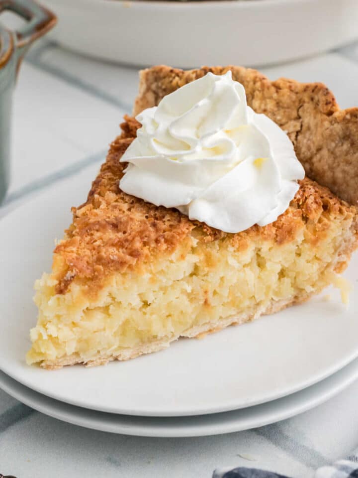 A slice of coconut pie with some cream squirted on top.