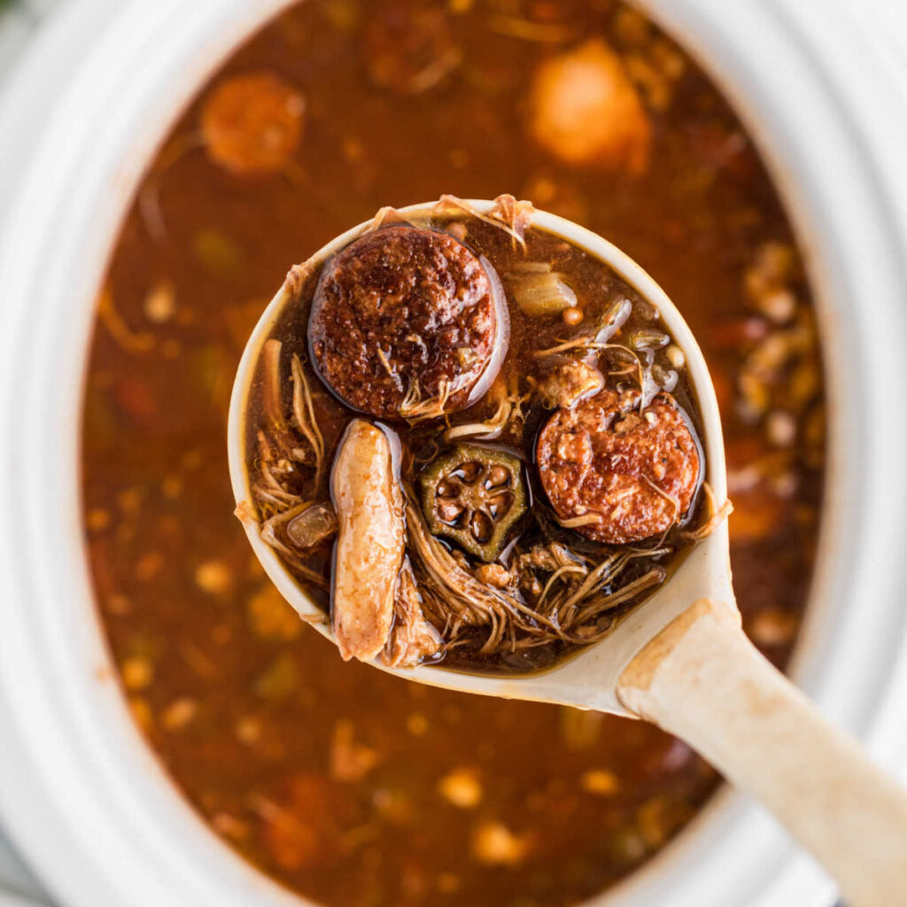 Overhead shot of a ladle coming out of a slow cooker with gumbo.