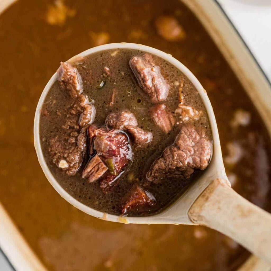 An overhead image of a pot of beef gumbo with a ladle spooning some out.