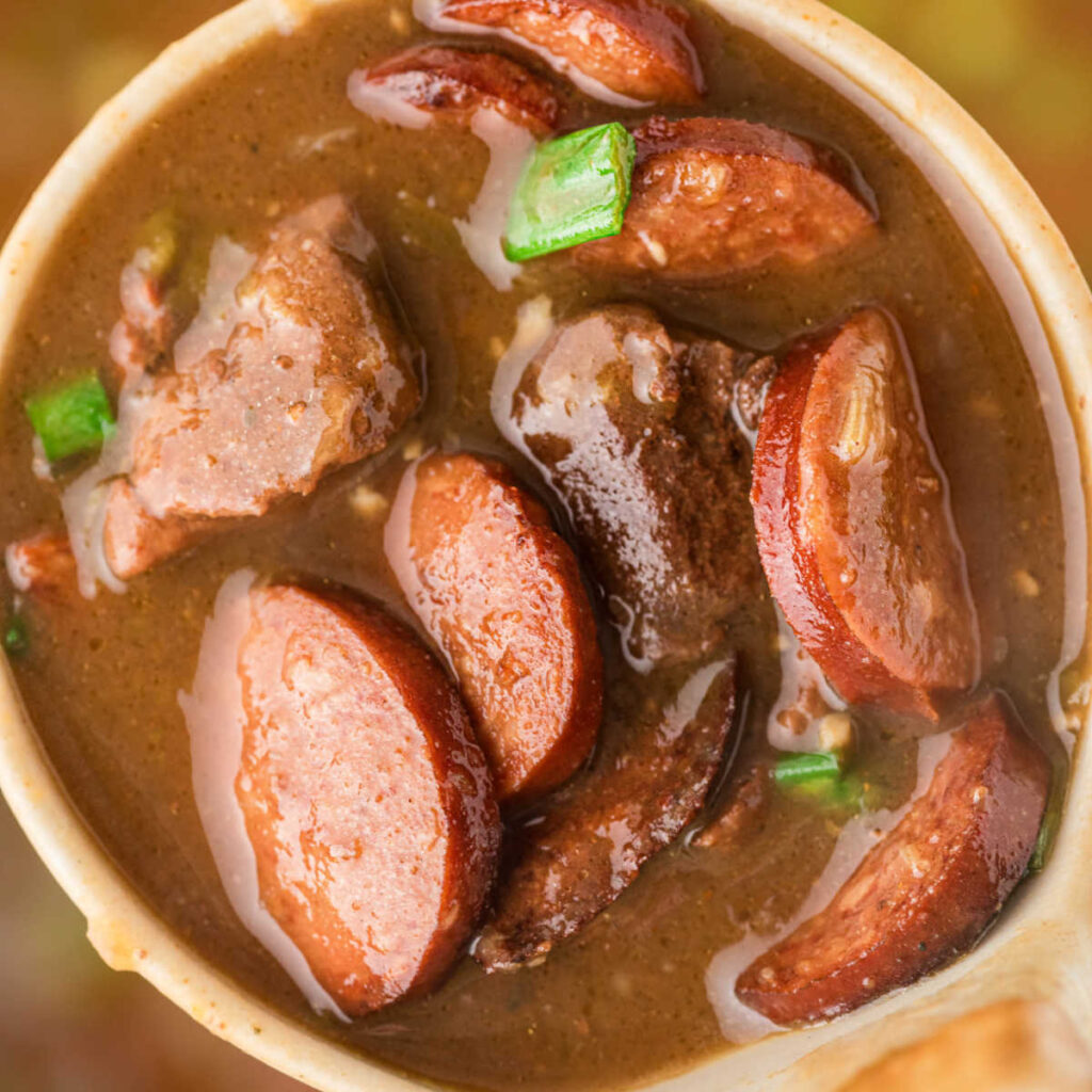 Image cropped square of a ladle full of poule d'eau gumbo with andouille sausage.