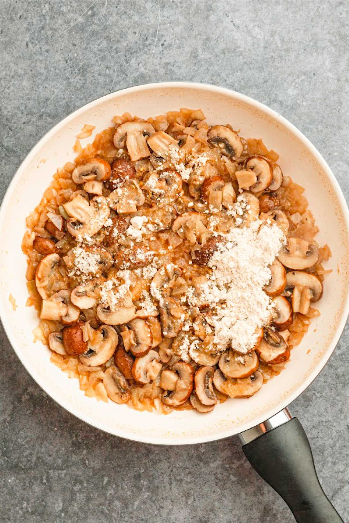 A large skillet with browned chicken, with flour added.