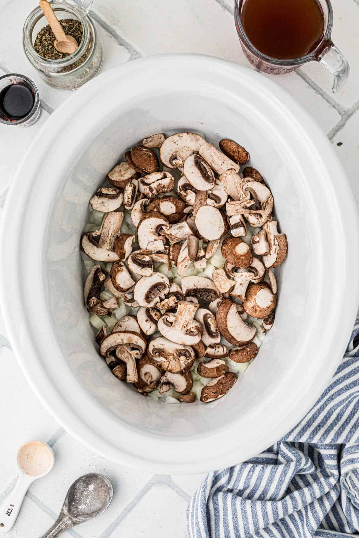 A large slow cooker filled with onions and mushrooms.