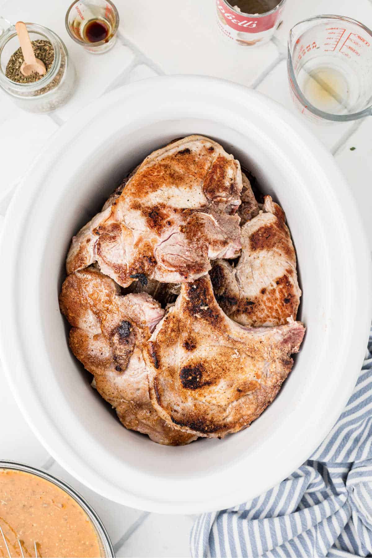 A slow cooker with seared pork chops.