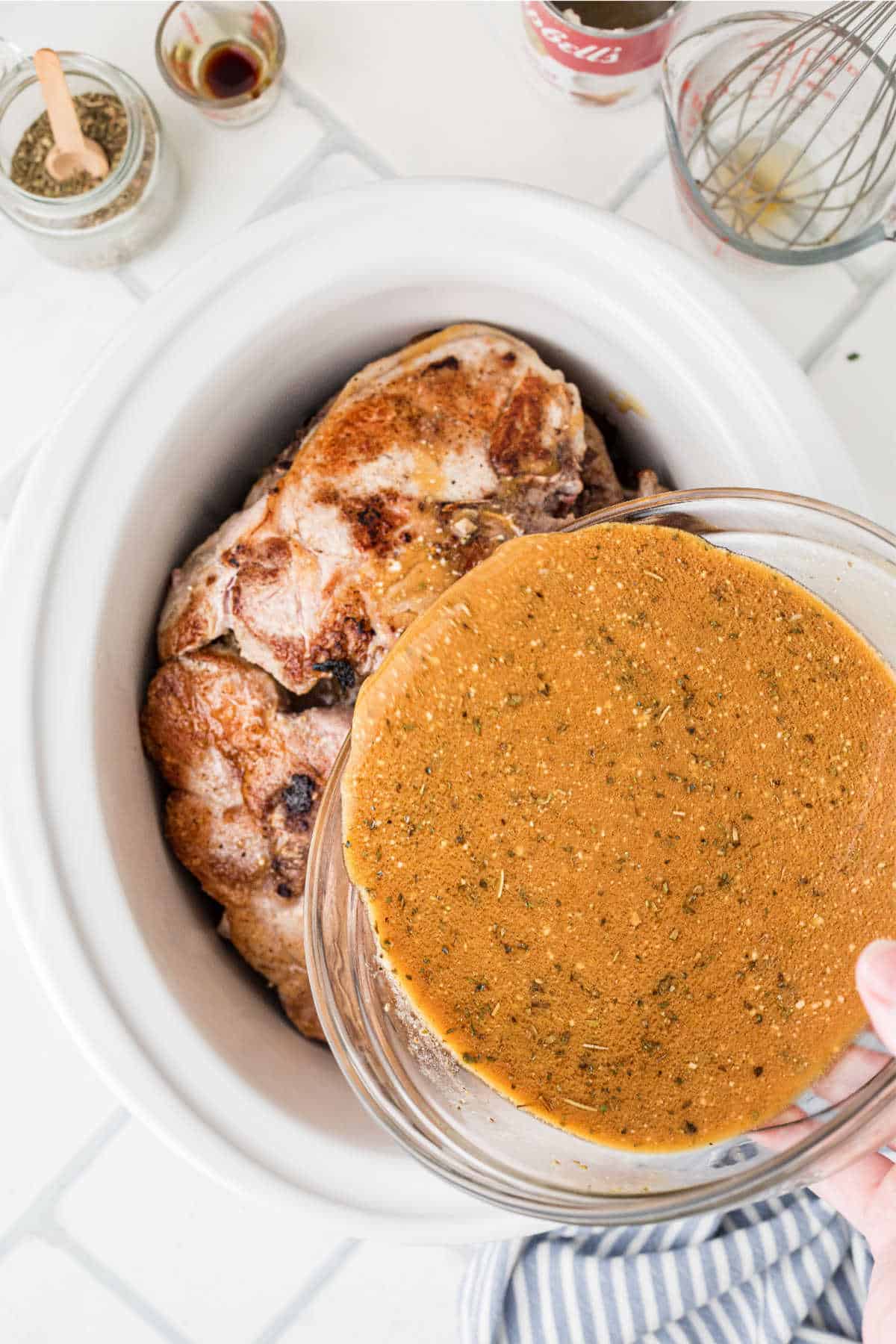 A large slow cooker with pork chops, a gravy is being poured over the top.