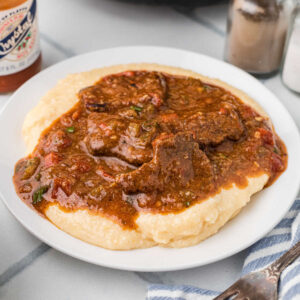 Close up of a plate of grillades and grits, the image has been cropped square.