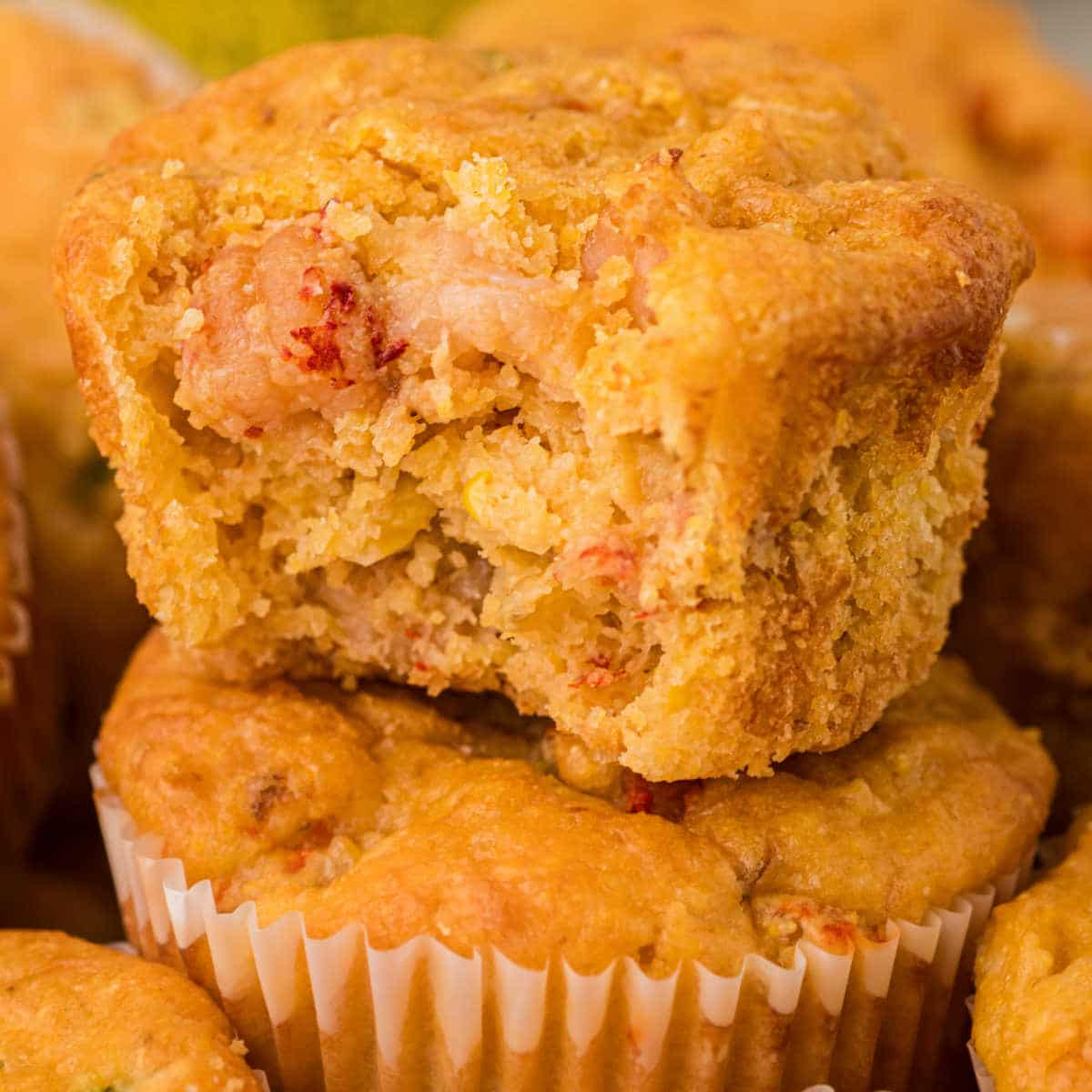 A crawfish cornbread muffin with a bite taken out of it, standing on top of another.