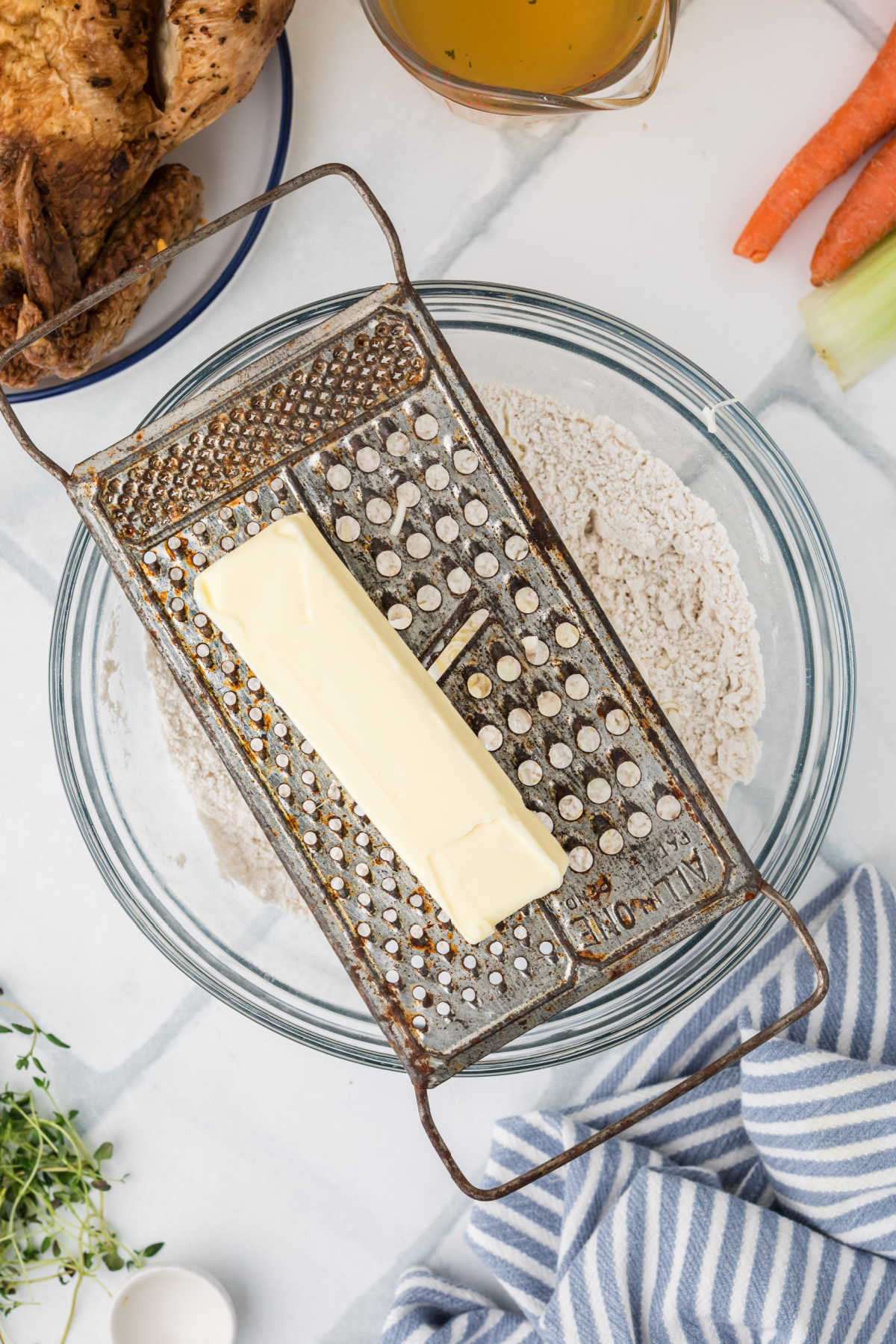 A grater with a stick of butter, being grated into a bowl of flour.
