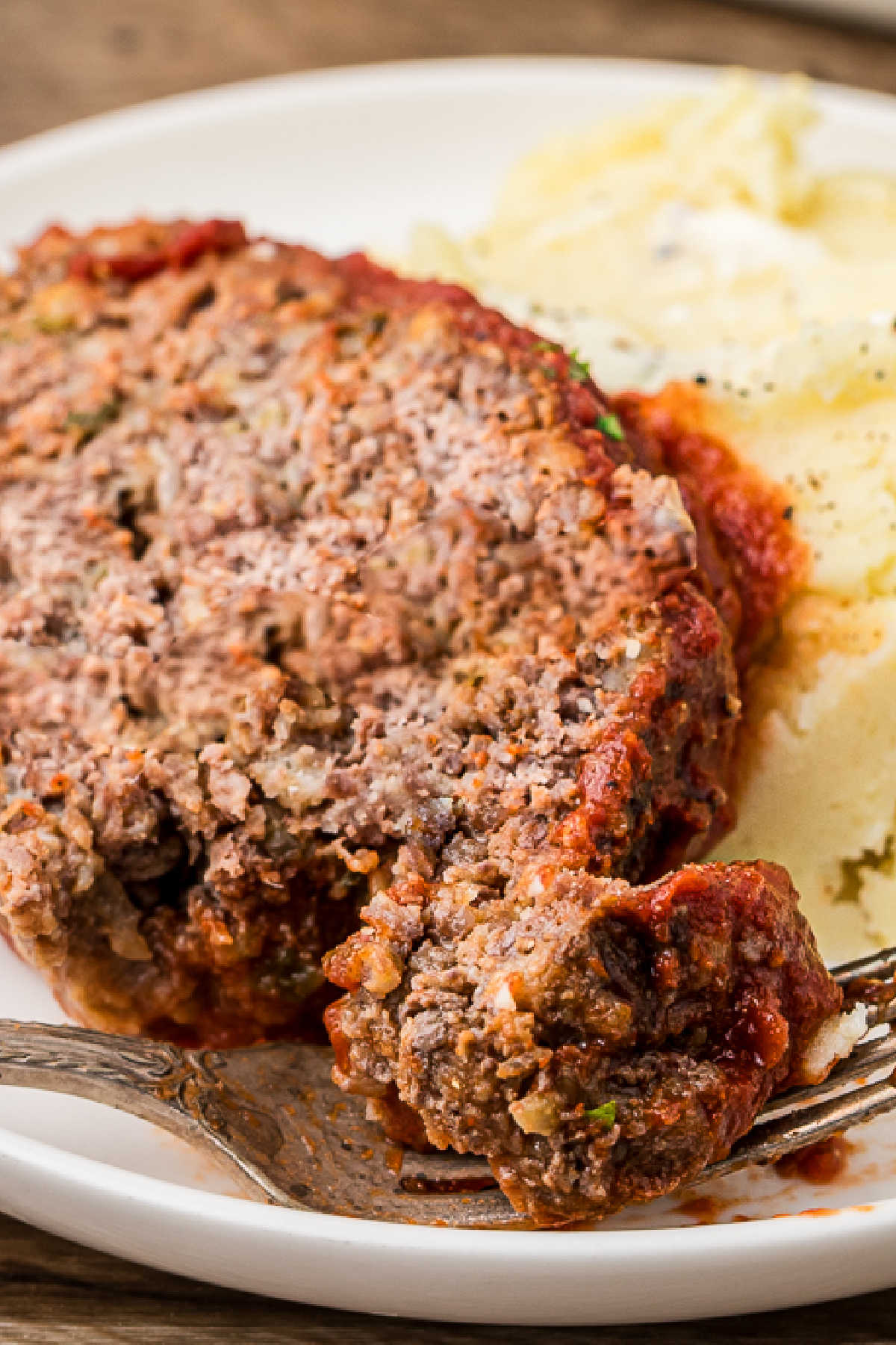 Close up view of a slice of Cajun meatloaf with mashed potatoes.