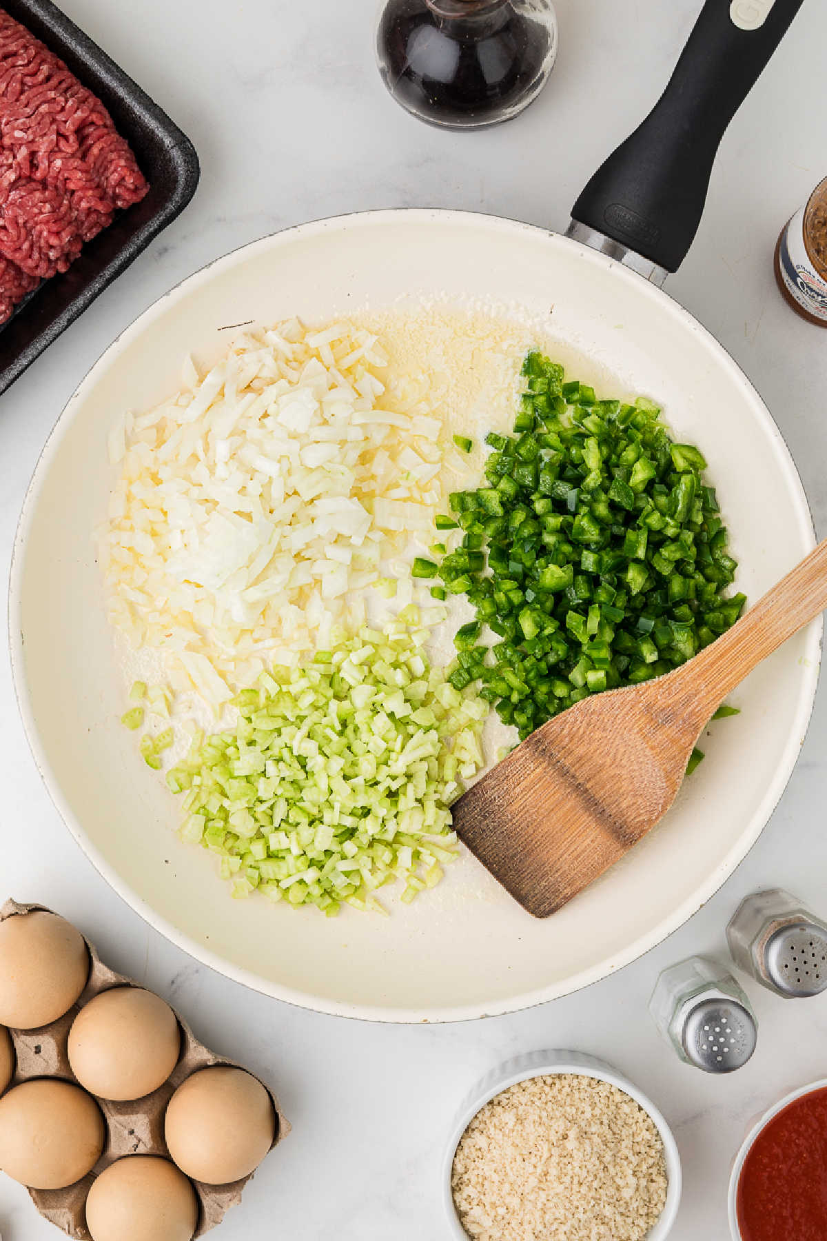 A large skillet with onions, bell peppers and celery.