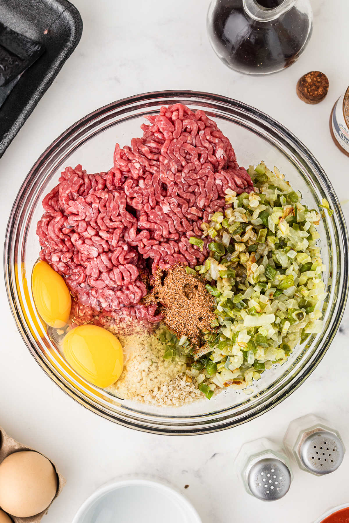 A large mixing bowl with ground beef, vegetables, breadcrumbs and eggs.