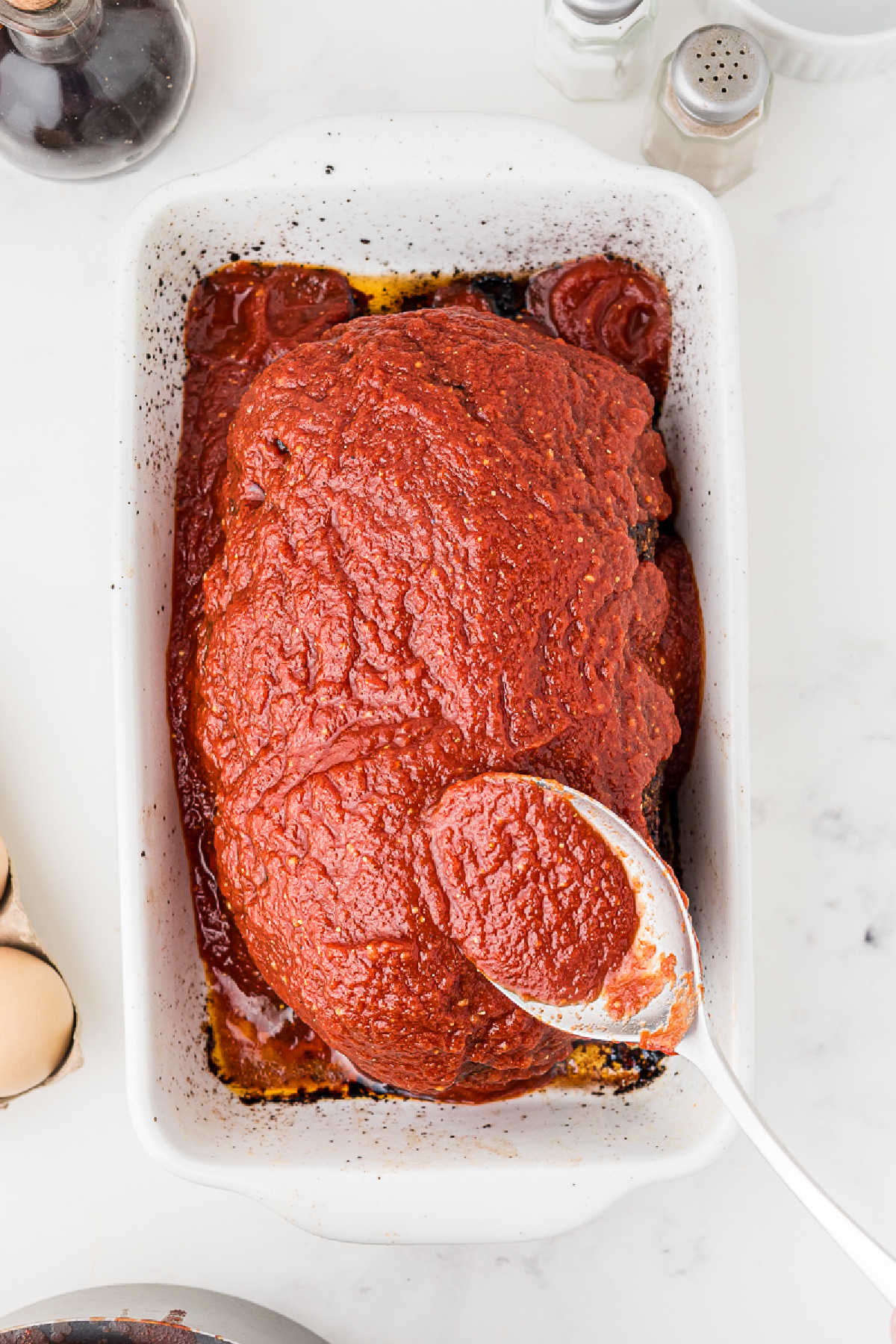 Tomato sauce being spread on top of a Cajun meatloaf.