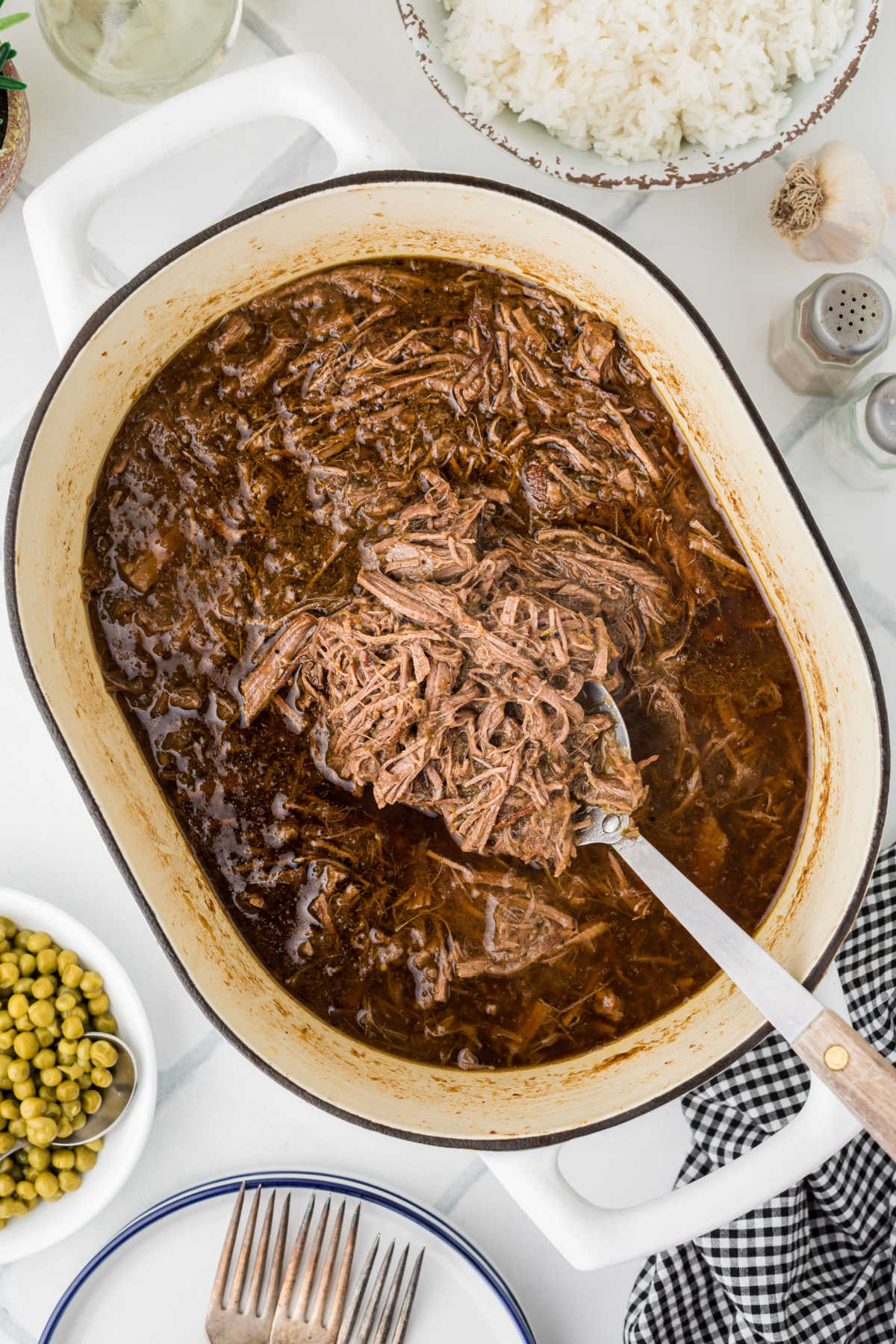 Overhead view of a pot with shredded roast, being spooned out.