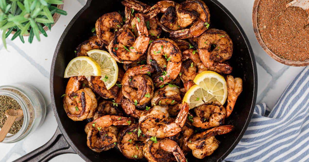 A cast iron skillet filled with blackened shrimp and lemon slices.