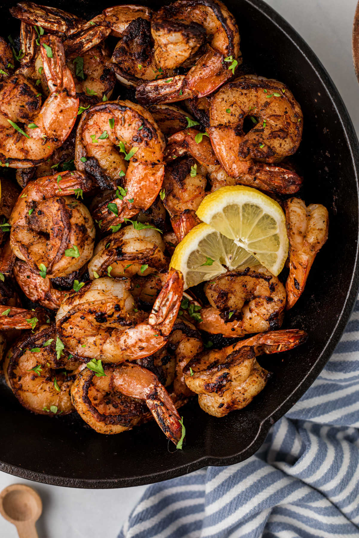 A close up shot of a cast iron skillet with Cajun Blackened Shrimp and lemon slices.