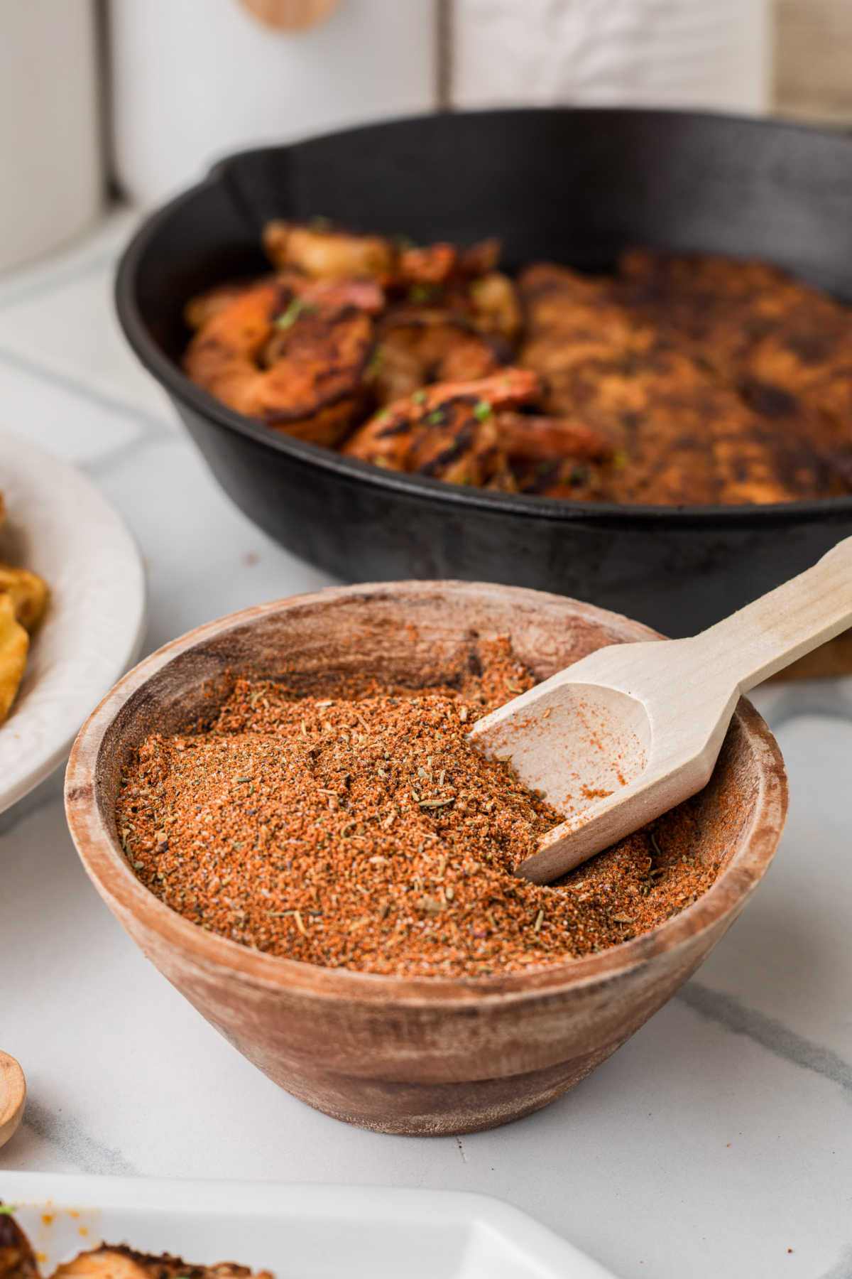 A small bowl with homemade blackened seasoning, with blackened chicken in the background cooking.