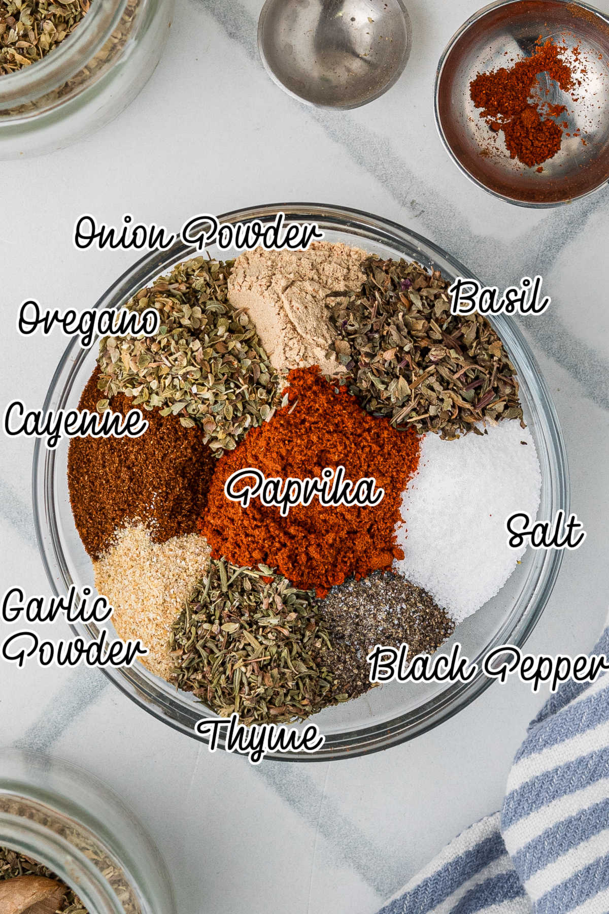 A glass mixing bowl filled with the herbs and spices needed to make homemade blackened seasoning.