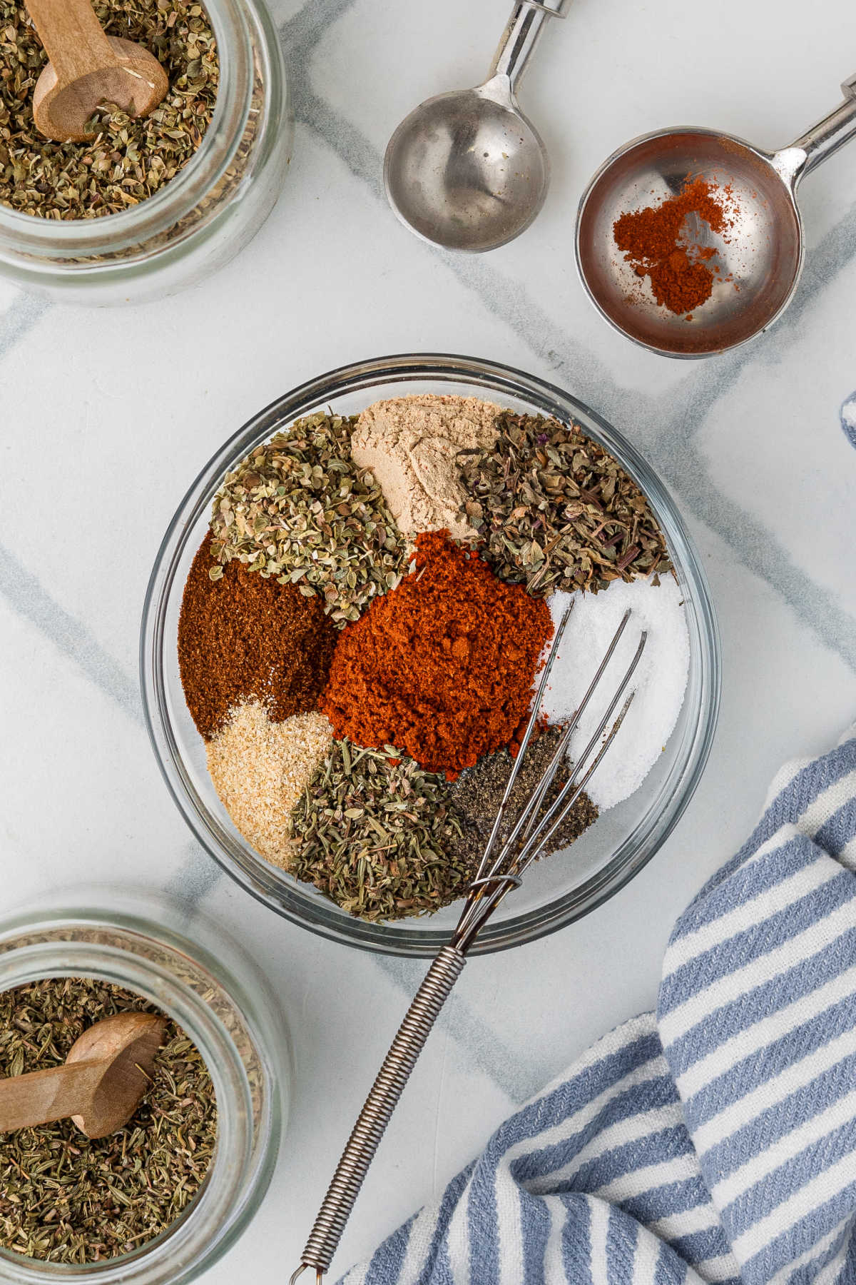 A glass bowl filled with herbs and spices about to be mixed up with a small whisk.