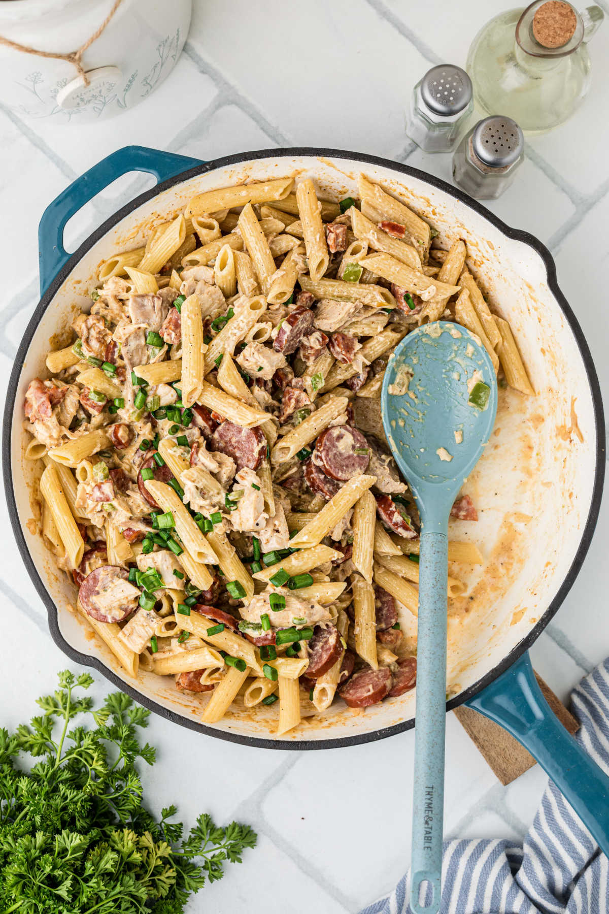 An overhead shot of a skillet with Cajun chicken and sausage pasta, with a spoon resting in a spot that's missing.