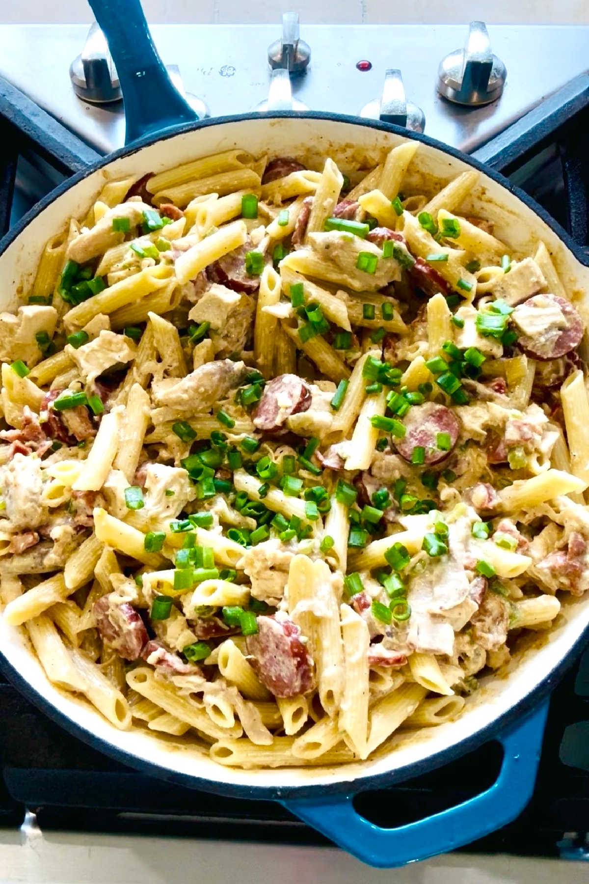 Green onions added to a large skillet of noodles, sausage and chicken.