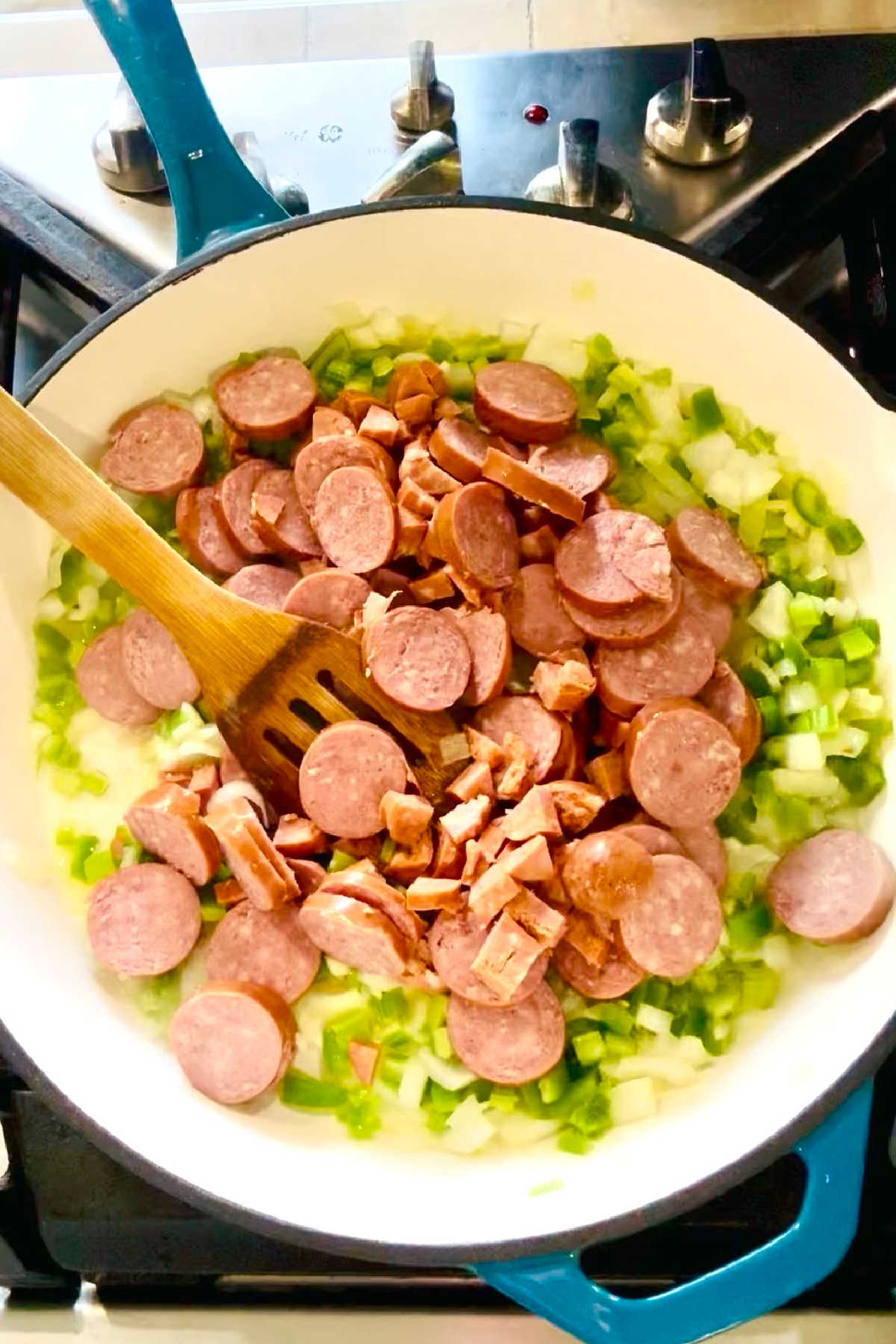 Slices of smoked sausage added to a large skillet with onions, bell peppers and celery.