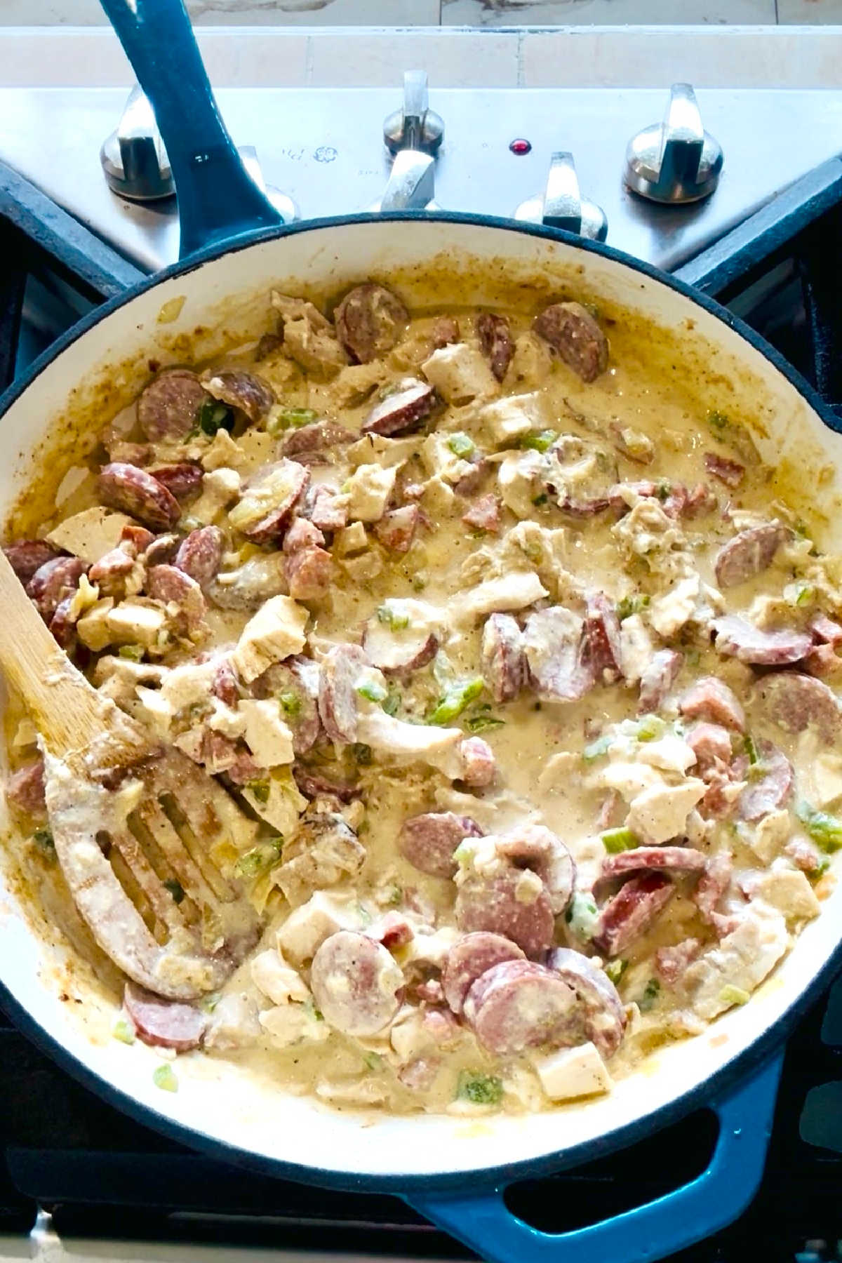 A large skillet with a creamy chicken and sausage sauce.
