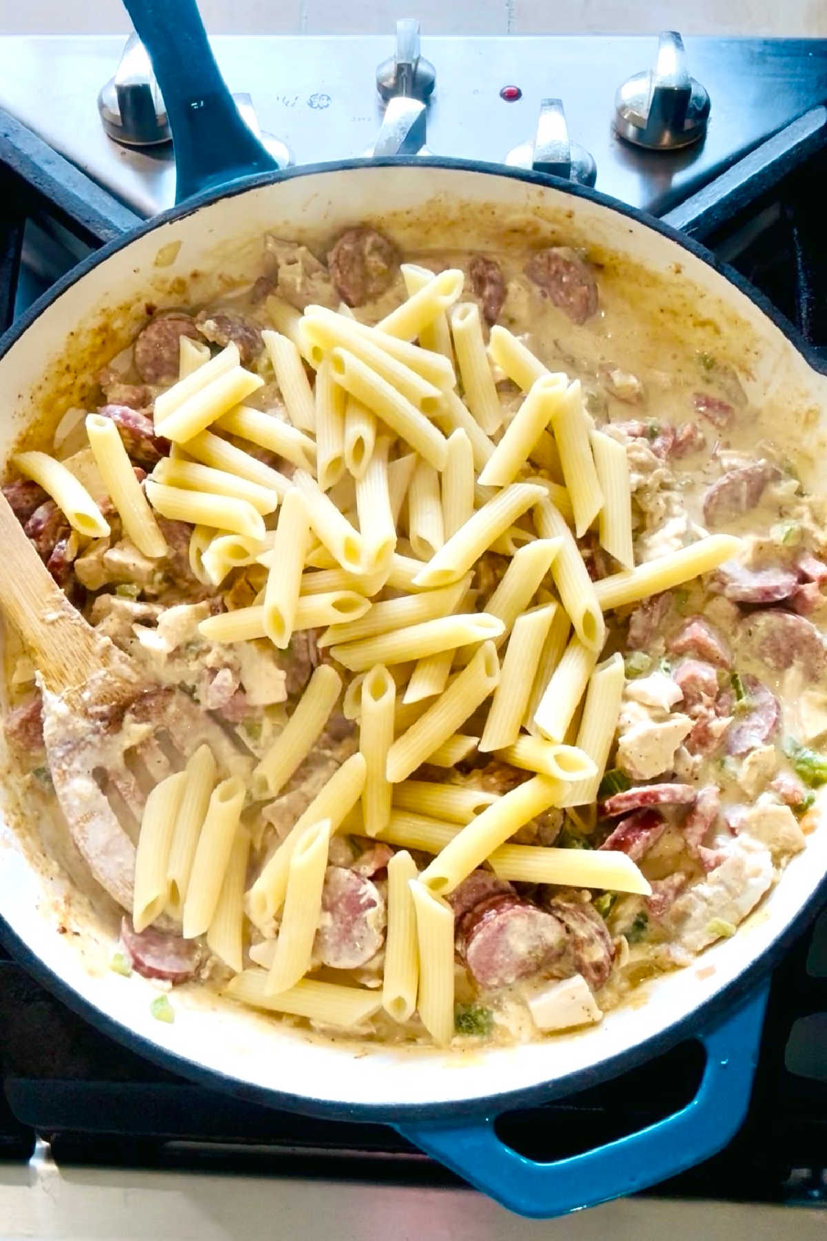 Cooked noodles being added to a large skillet.