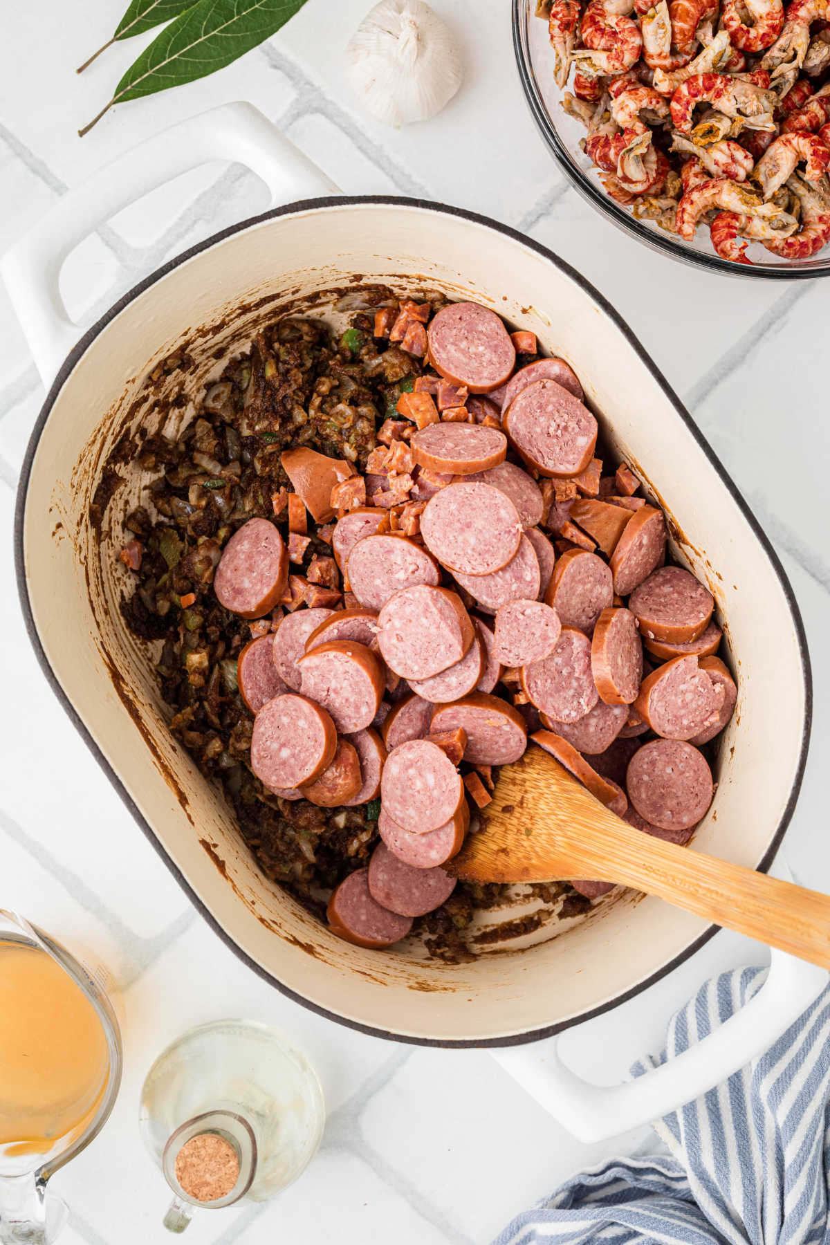 Sliced smoked sausage added to a pot with roux and vegetables.