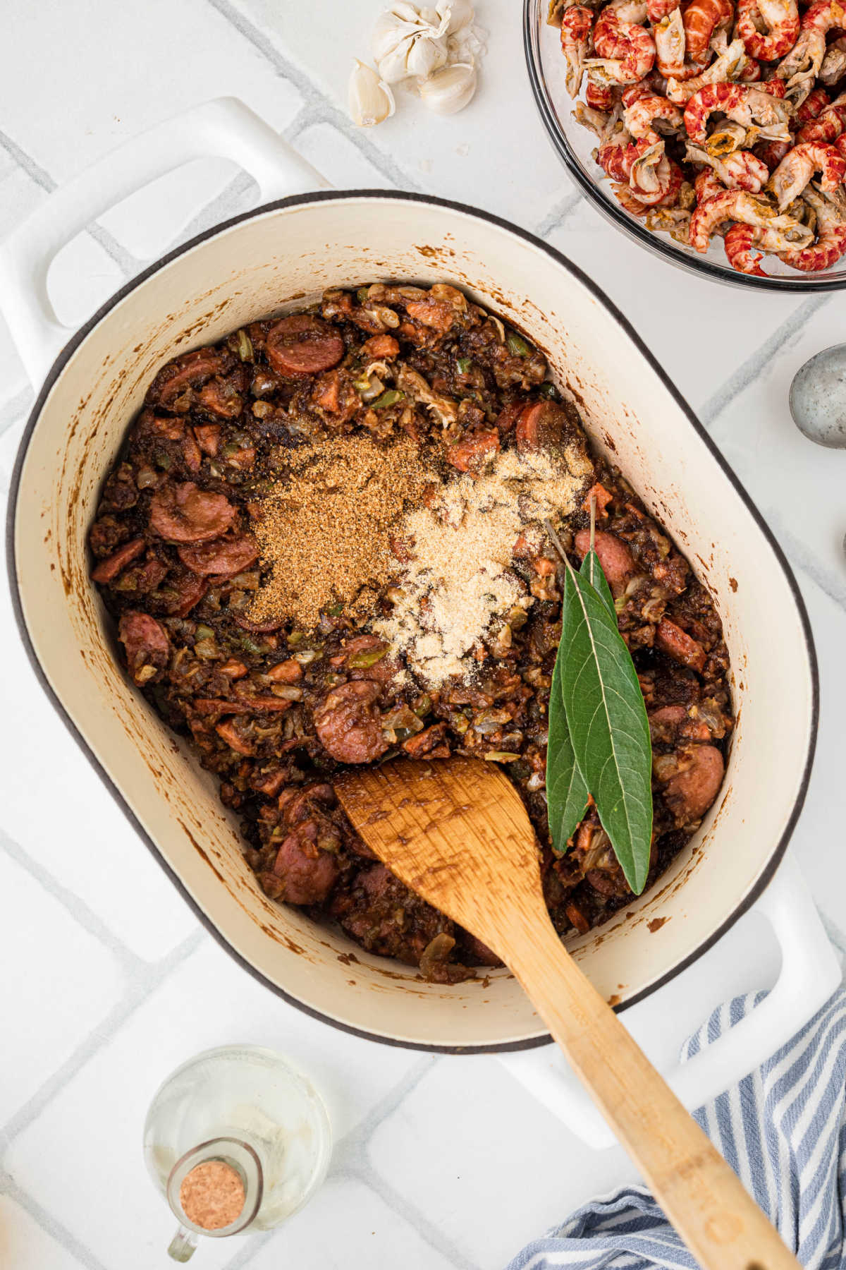 Seasonings and bay leaves added to a pot with a roux, veggies and smoked sausage.