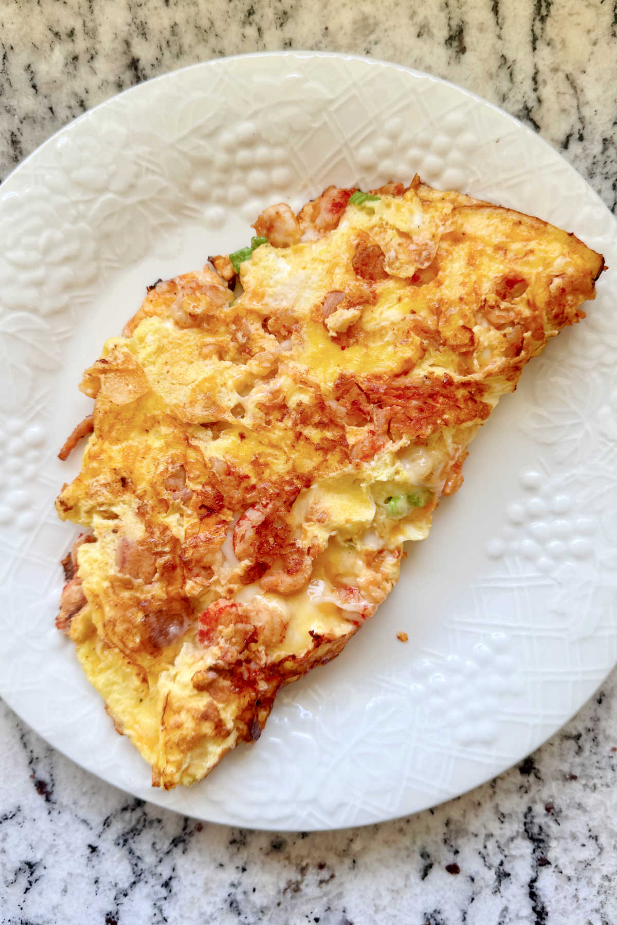 A cheesy crawfish omelette on a white plate.
