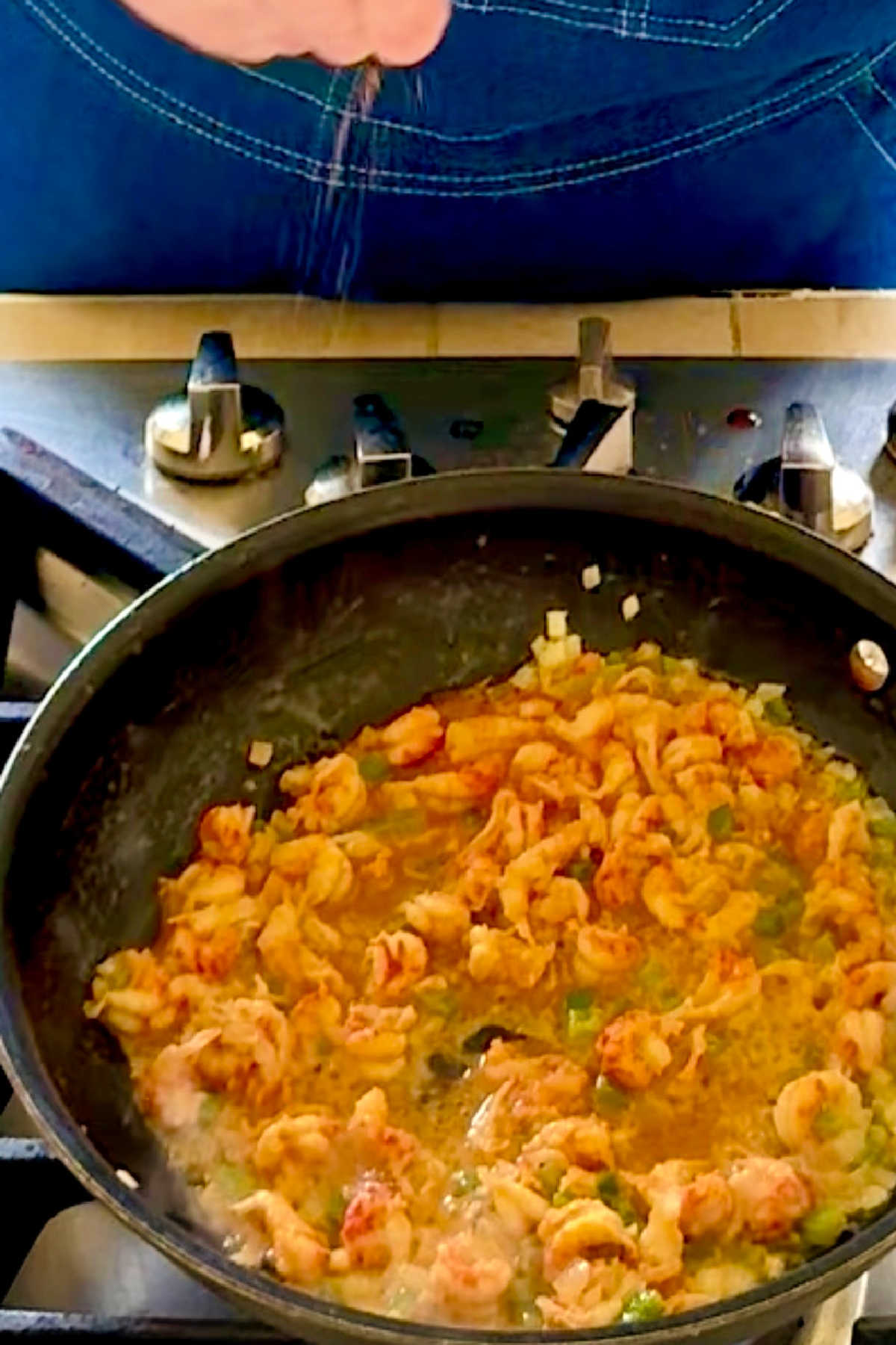 Seasoning being sprinkled into a skillet of crawfish and onions.