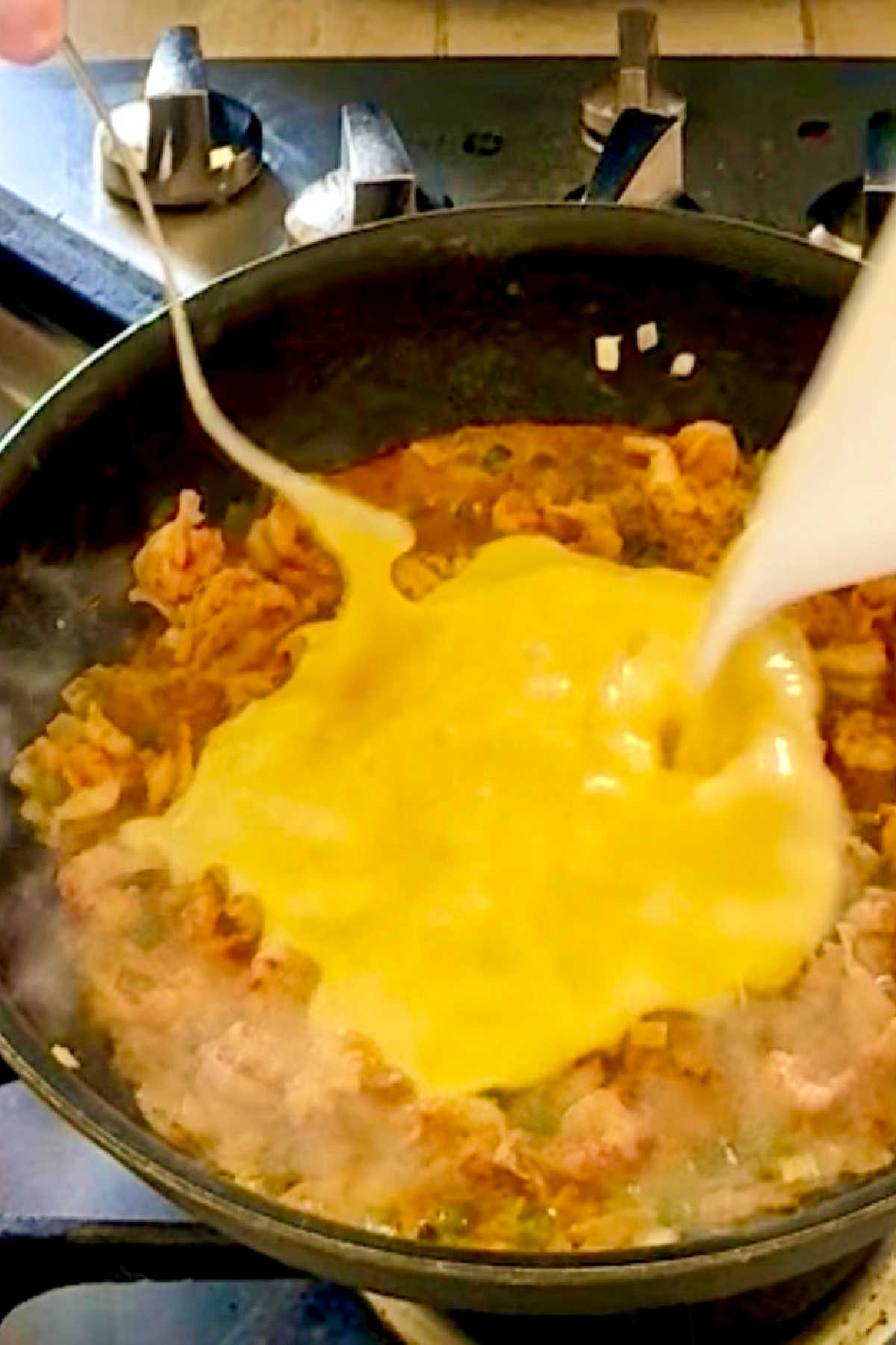 Beaten eggs being added to a skillet with crawfish tails and vegetables.