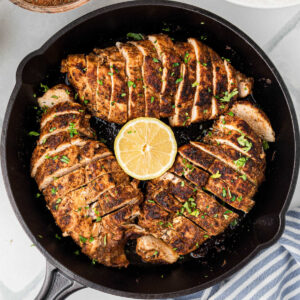 Overhead of a black skillet with three blackened chicken breasts, sliced into even pieces.