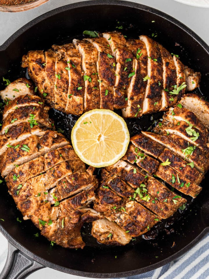 Overhead of a black skillet with three blackened chicken breasts, sliced into even pieces.